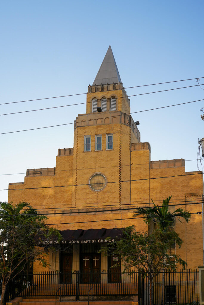 Historical St. John Baptist Church in Overtown at golden hour — yellow-brick facade with pyramidal steeple